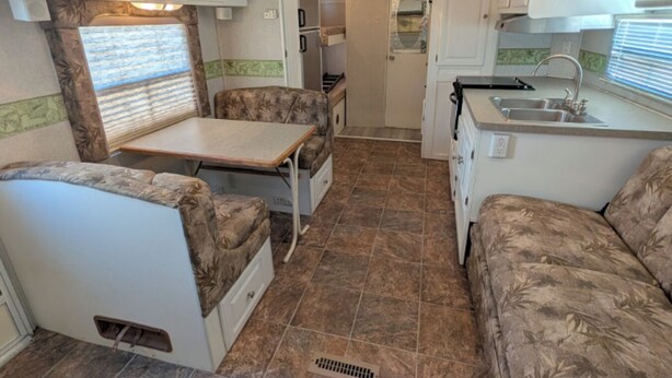 Een compact interieur van een camper met een kitchenette, een eethoek en een zithoek.