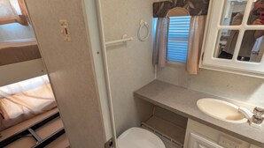Een kleine badkamer in een camper, met toilet, wastafel en spiegel.