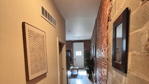 A hallway with wooden flooring, a brick wall, and framed artwork on the walls. - Benton Park Walkable Apartment- IN1S (St. Louis)