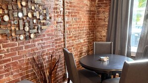 A room with a brick wall, a round table with chairs, a small cabinet, and a window with curtains. - Benton Park Walkable Apartment- IN1S (St. Louis)