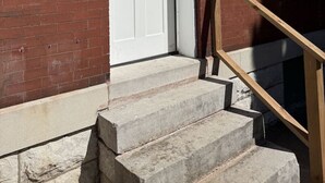 A red brick building with a white door, a small set of concrete steps, and a wooden handrail. - Benton Park Walkable Apartment- IN1S (St. Louis)