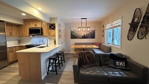 A modern kitchen with wooden cabinets, a central island, and a dining area with a bench and chairs. - Cozy 3-bedroom townhome in West Dover, steps from the magic carpet (Dover)