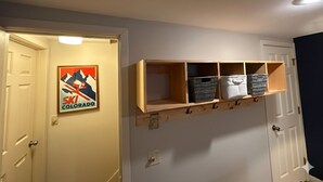 A hallway with a ski-themed poster, a wooden shelf with storage baskets, and a white door. - Cozy 3-bedroom townhome in West Dover, steps from the magic carpet (Dover)