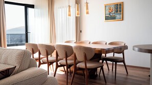 A modern dining area with a wooden table and chairs, a painting on the wall, and a view of the outdoors. - Villa Isabel Azure  (Matulji)