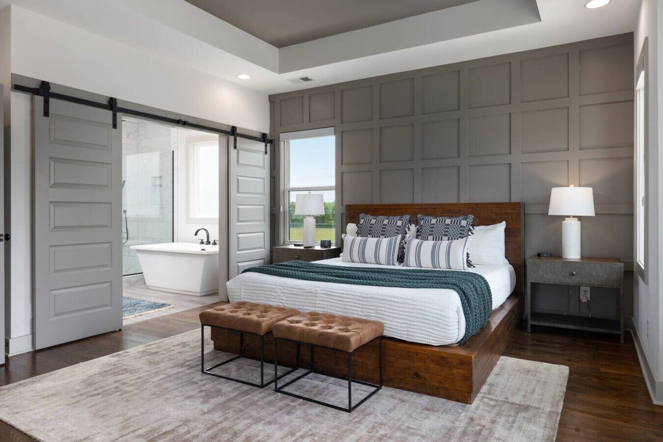 Een slaapkamer met een groot bed, een houten bankje, een nachtkastje, een lamp en uitzicht op een badkamer.