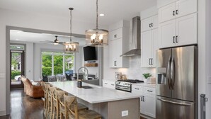 A modern kitchen with a large island, stainless steel appliances, and a dining area with wooden chairs. - House with Rooftop Patio, Next to a Park, 3 Miles to Downtown (Nashville)
