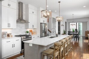 A modern kitchen with white cabinets, stainless steel appliances, and a central island with bar stools. - House with Rooftop Patio, Next to a Park, 3 Miles to Downtown (Nashville)