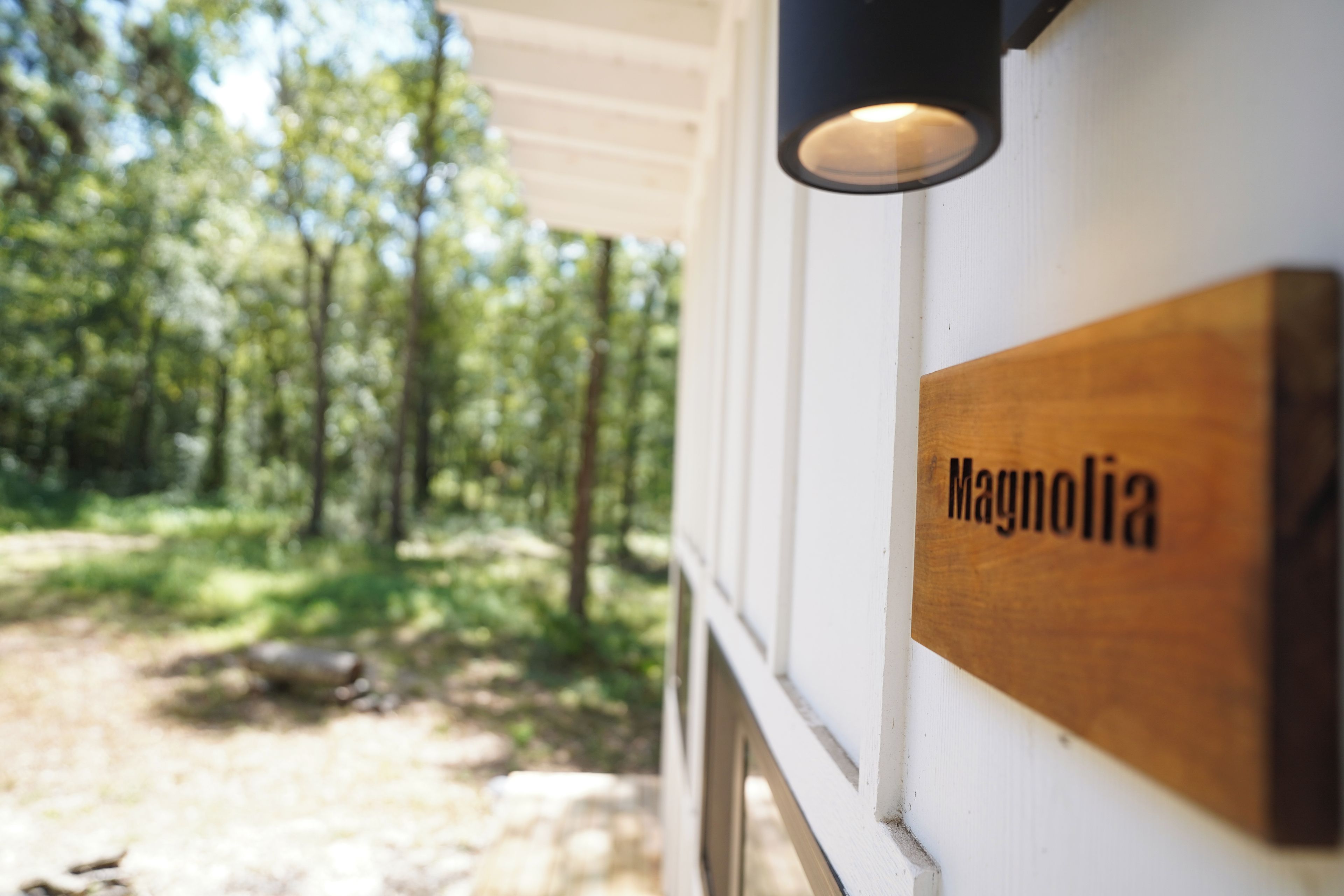 A wooden sign with the name 'Magnolia' on a white wall, with a forested area in the background.