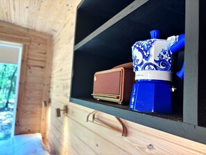 A wooden interior with a shelf containing a blue and white ceramic mug, a brown radio, and a blue water bottle.