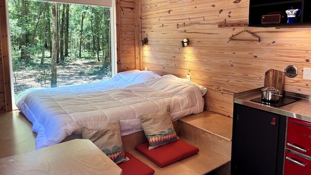 L’intérieur d’un chalet en bois comprend un lit, une petite table, un buffet rouge et une fenêtre donnant sur une forêt.
