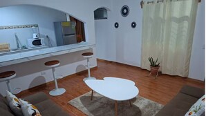A living room with a sofa, a coffee table, a kitchen area with a microwave and refrigerator, and a potted plant. - Villa Ensueño Cahuita 2 familiar (Westfalia)
