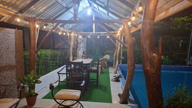 A covered outdoor area with a pool, wooden furniture, and string lights. - Alojamientos Ensueño Cahuita 1 (Westfalia)