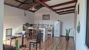 A kitchen with a dining area, wooden chairs, a table, a refrigerator, and potted plants. - Alojamientos Ensueño Cahuita 1 (Westfalia)