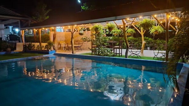 Un espace piscine aménagé pour la nuit, avec des guirlandes lumineuses, du mobilier d’extérieur et des plantes en pot.