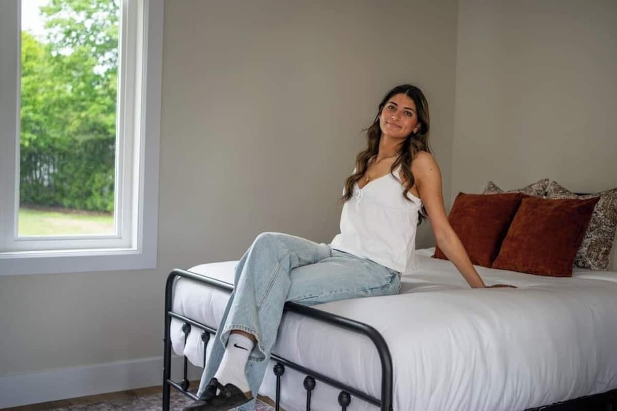 A bed with a metal frame, white bedding, and a window with a view of trees.