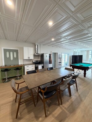 Una habitación amplia con una mesa de comedor, sillas, una mesa de billar y una zona de cocina.