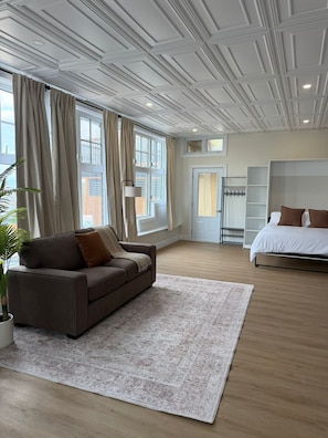 Un dormitorio moderno con sofá, cama, ventanal grande y techo con diseño de cuadrícula.