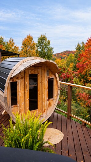 A wooden cabin with a curved roof, a wooden deck, and a view of autumn foliage.