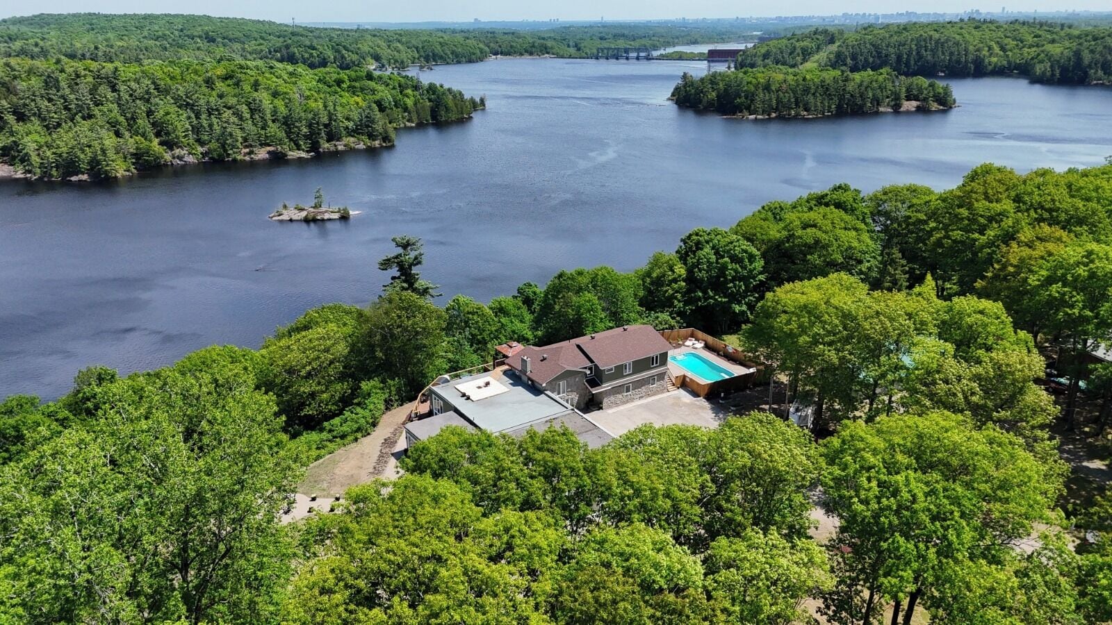 Una casa con piscina, rodeada de un bosque frondoso y una gran masa de agua.