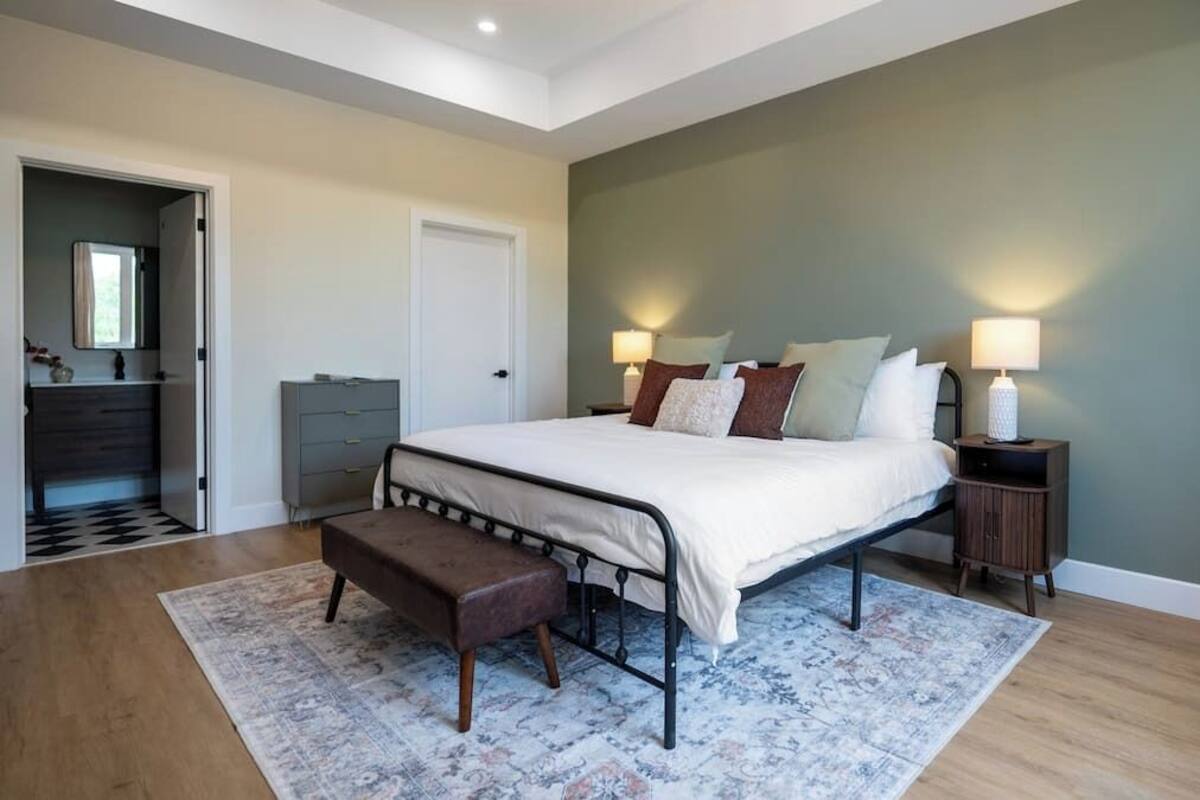 A bedroom with a bed, bedside tables, a bench, a rug, and a door.