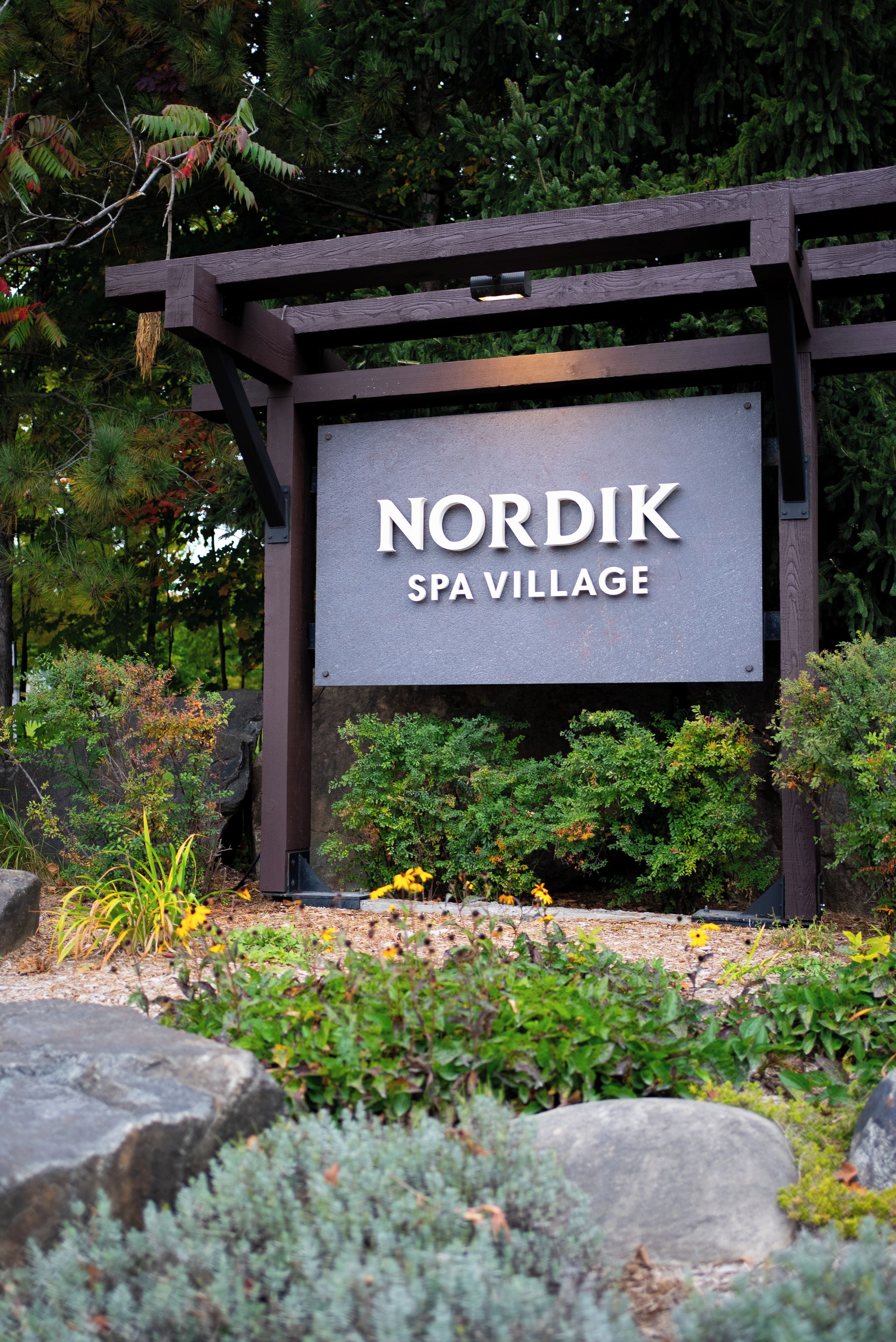 A sign for 'Nordik Spa Village' with a wooden frame and a grey background.