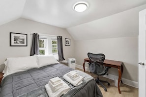 A bedroom with a bed, a desk, a chair, and a window with curtains.