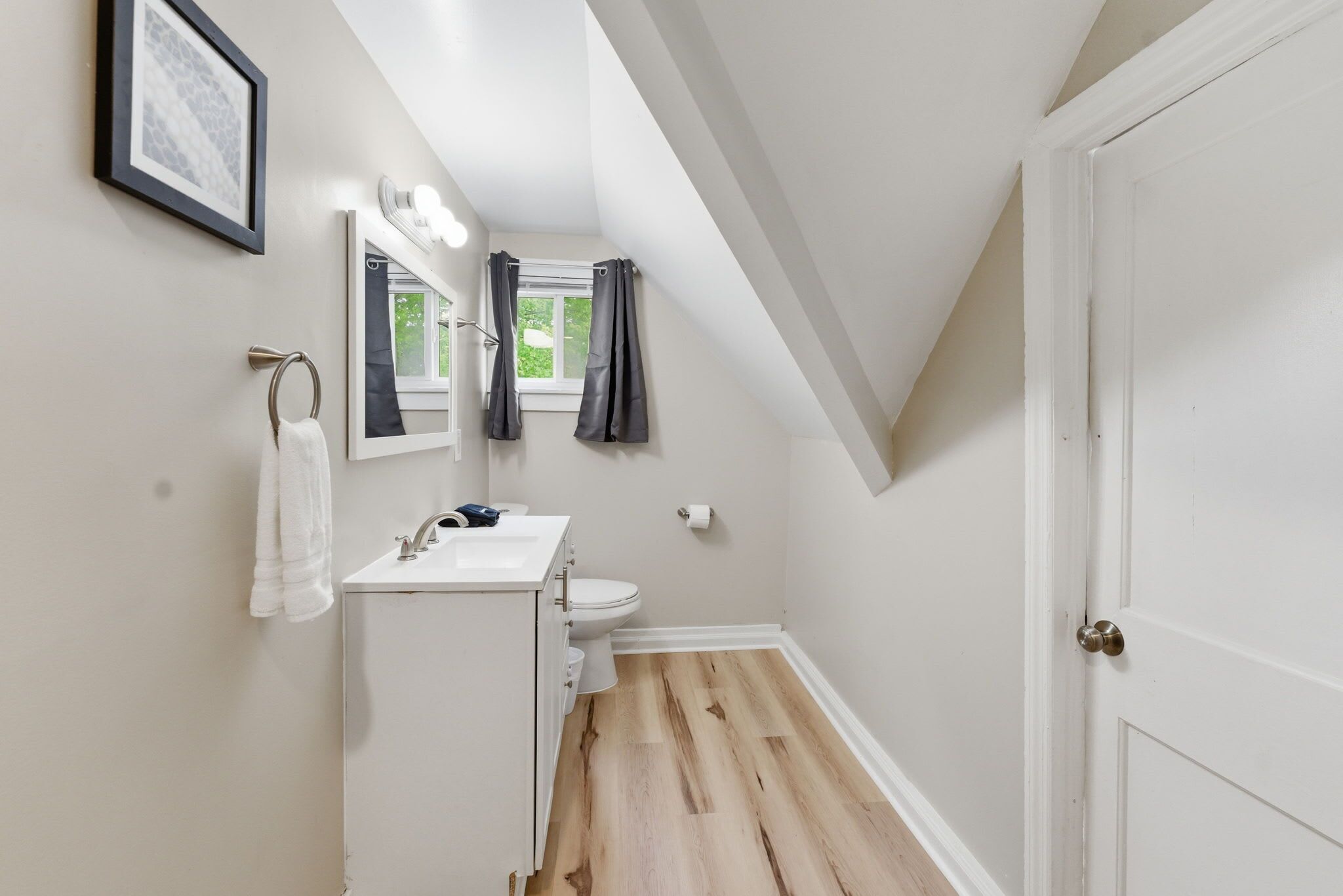 Een badkamer met een witte wasbak, spiegel en toilet, houten vloer en een deur met een messing knop.