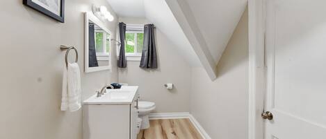 Een badkamer met een witte wasbak, spiegel en toilet, houten vloer en een deur met een messing knop.