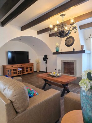 Una sala de estar con televisión, sofá, mesa de centro, chimenea y elementos decorativos.