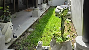 Une cour avec un sol carrelé, des plantes en pot et une statue.