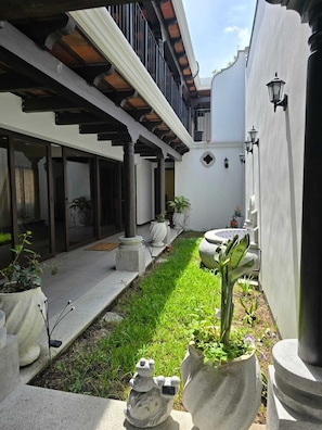 Une cour avec un sol carrelé, des plantes en pot et une statue.