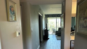 Un couloir avec un plancher en bois, une porte donnant sur un balcon et un tableau encadré accroché au mur.