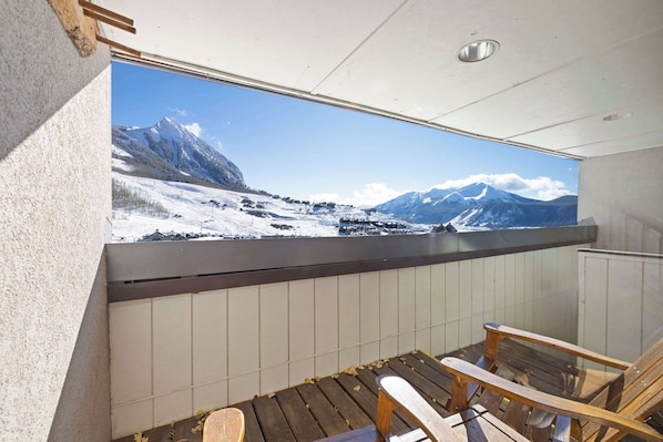 A room with a large window overlooking a snowy mountain landscape. There is a wooden bench and a radiator.