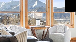 A room with large windows, a flat-screen TV, and a table with a lamp. - Traverse Hospitality (Crested Butte)