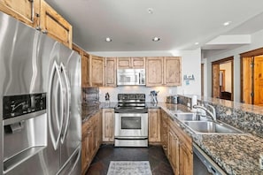 A modern kitchen with stainless steel appliances, wooden cabinets, granite countertops, and a built-in oven.
