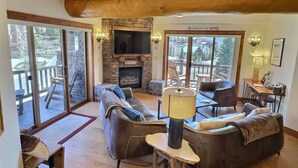A cozy living room with a stone fireplace, leather sofas, and a large TV. - Traverse Hospitality (Crested Butte)