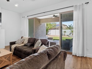 Ein modernes Wohnzimmer mit einer Couch, einem Holztisch und einer Schiebeglastür, die zu einer Außenpatio führt.