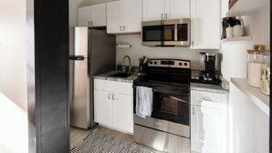 A modern kitchen with stainless steel appliances, white cabinetry, and a patterned rug.
