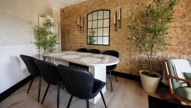 A modern kitchen with a brick wall, a large window, and a dining table with chairs.