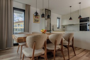 Eine moderne Küche mit Essbereich, Holzmöbeln, Pendelleuchten und Blick auf Gebäude.