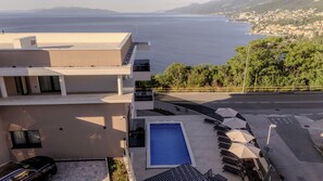 Ein modernes Gebäude mit Pool auf dem Dach, Sitzgelegenheiten im Freien und Blick aufs Meer.