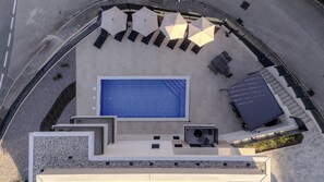 Luchtbeeld van een zwembadterras met een groot zwembad, ligbedden, parasols en een overdekt zitgedeelte.