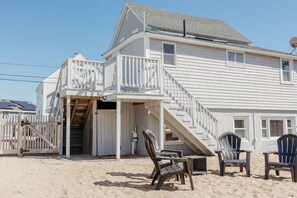 Ein Strandhaus mit Balkon, einer Treppe zum Hauptgeschoss und Strandliegen.