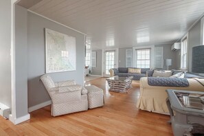 Ein geräumiges Wohnzimmer mit großem Fenster, einer Karte an der Wand und einem Sofa mit einem 'BEACH'-Kissen.