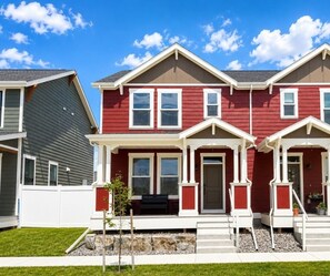 A two-story residential building with a red exterior, white trim, and a front porch with steps. - Moss & Blush-King Bed-Garage (Billings)