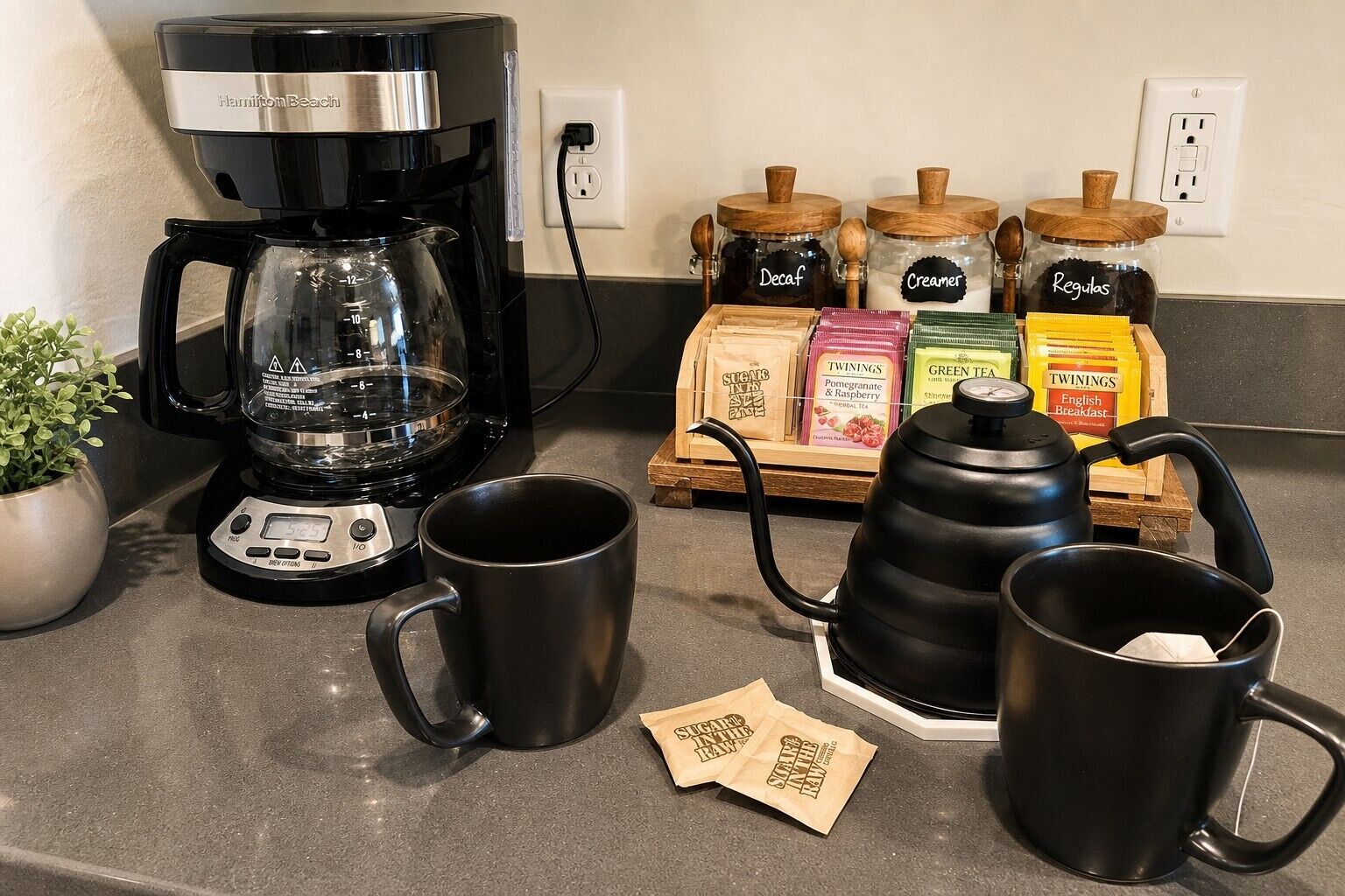 A kitchen counter with a coffee maker, two mugs, a kettle, and various food items.