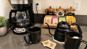 A kitchen counter with a coffee maker, two mugs, a kettle, and various food items.