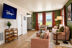 A living room with a flat-screen TV displaying the Disney+ logo, a sofa set, a coffee table, and a potted plant.