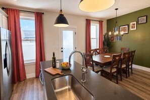 A modern kitchen with a central island, stainless steel sink, and a dining area with wooden chairs and a table.