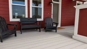 En veranda med tre Adirondack-stolar, en bänk och en dörr med ett nummer på.